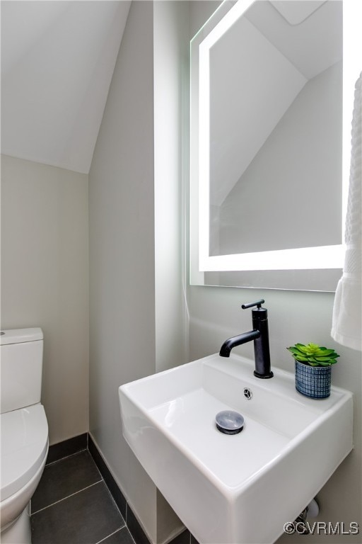 bathroom with tile patterned flooring, sink, toilet, and vaulted ceiling