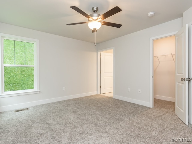 unfurnished bedroom featuring a spacious closet, light colored carpet, a closet, and ceiling fan