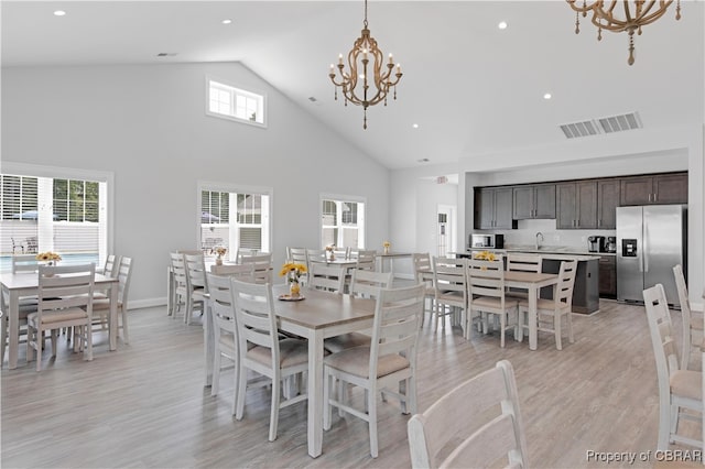 dining area with a notable chandelier, high vaulted ceiling, light hardwood / wood-style flooring, and plenty of natural light