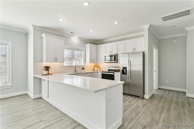 kitchen with ornamental molding, white cabinets, stainless steel appliances, and light wood-type flooring