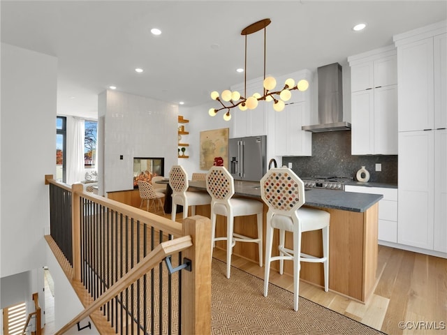 kitchen featuring high end refrigerator, wall chimney range hood, white cabinets, light hardwood / wood-style floors, and a kitchen island