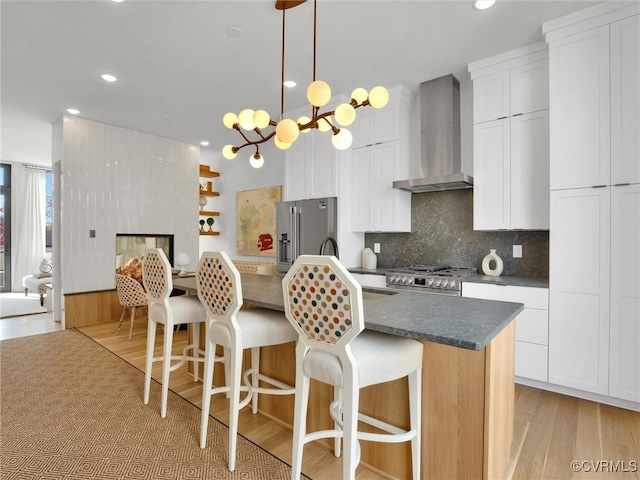 kitchen featuring wall chimney range hood, light hardwood / wood-style flooring, high quality appliances, a center island, and white cabinetry