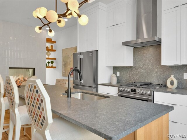 kitchen featuring wall chimney range hood, sink, decorative backsplash, premium appliances, and white cabinetry