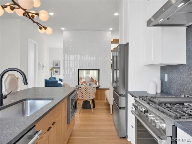 kitchen with white cabinetry, sink, wall chimney exhaust hood, light hardwood / wood-style floors, and appliances with stainless steel finishes