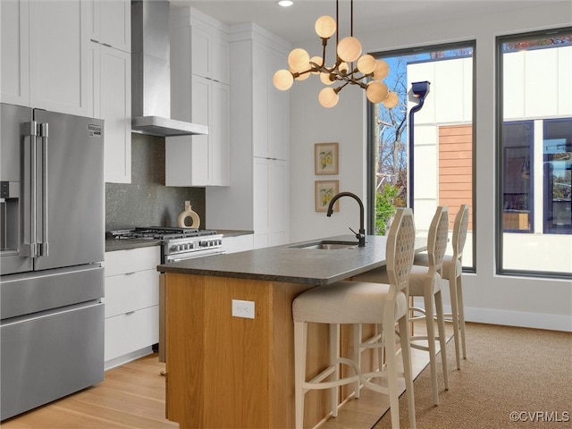 kitchen featuring high quality fridge, white cabinetry, an island with sink, and wall chimney range hood