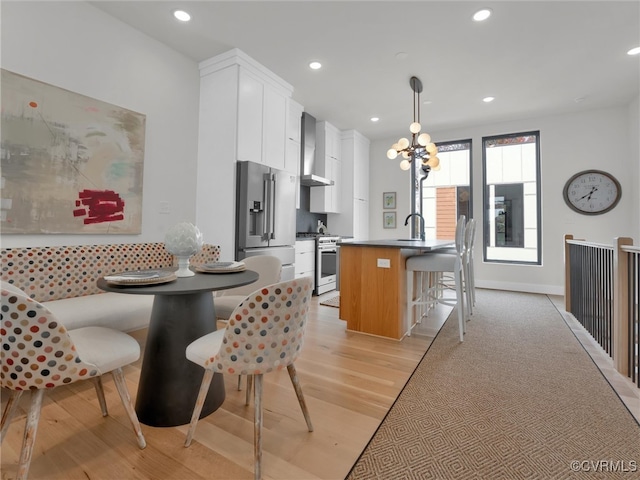 kitchen with hanging light fixtures, stainless steel appliances, wall chimney range hood, white cabinets, and light wood-type flooring