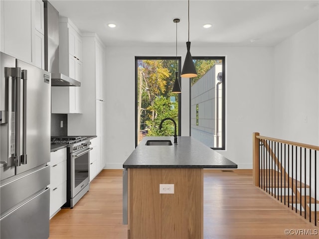 kitchen with wall chimney exhaust hood, an island with sink, hanging light fixtures, sink, and premium appliances