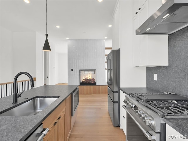 kitchen with wall chimney exhaust hood, hanging light fixtures, sink, white cabinetry, and appliances with stainless steel finishes