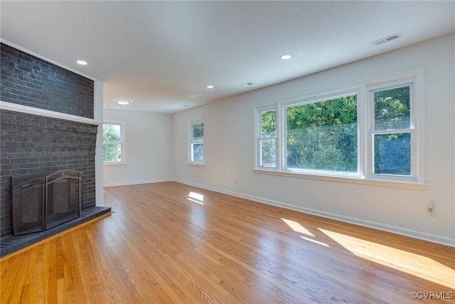 unfurnished living room with a brick fireplace, light hardwood / wood-style flooring, and a wealth of natural light