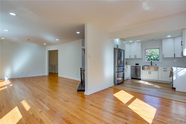 kitchen with light hardwood / wood-style flooring, stainless steel appliances, white cabinetry, and tasteful backsplash