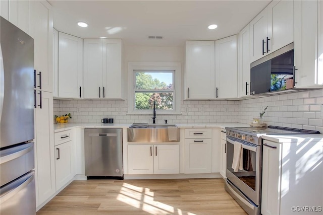 kitchen with stainless steel appliances, white cabinets, sink, and backsplash