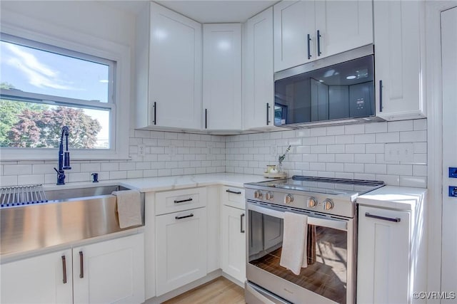 kitchen featuring white cabinets, stainless steel electric range, backsplash, and sink