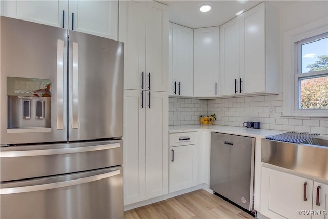 kitchen with light stone countertops, stainless steel appliances, light hardwood / wood-style floors, tasteful backsplash, and white cabinetry