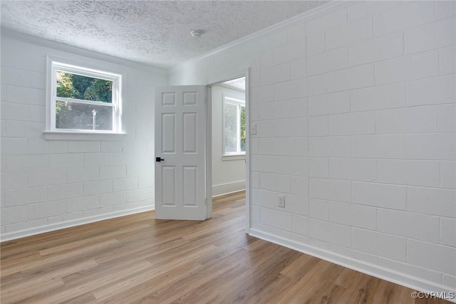 unfurnished room featuring a textured ceiling, light wood-type flooring, and crown molding