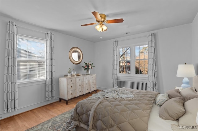 bedroom with radiator heating unit, multiple windows, wood-type flooring, and ceiling fan