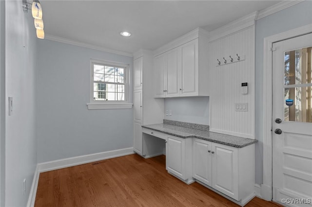 interior space featuring ornamental molding, built in desk, and light hardwood / wood-style flooring