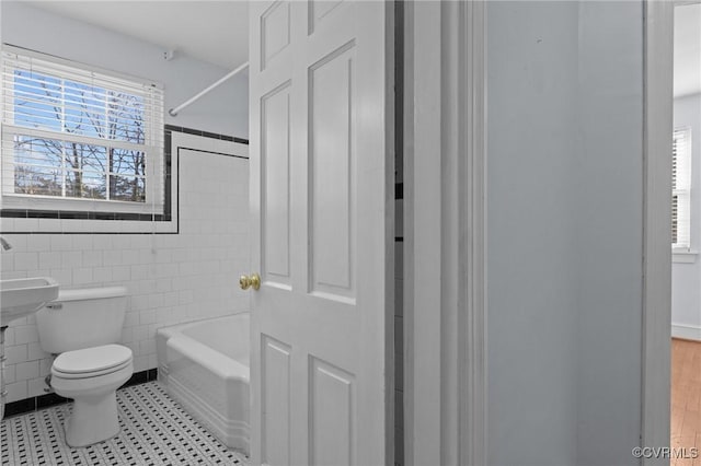 bathroom with toilet, tile walls, plenty of natural light, and shower / bathing tub combination