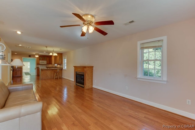 unfurnished living room featuring ceiling fan with notable chandelier and light wood-type flooring