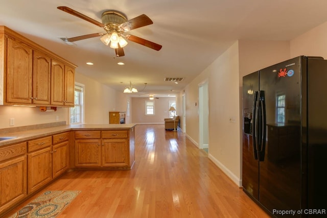 kitchen featuring a chandelier, light hardwood / wood-style flooring, kitchen peninsula, and black fridge