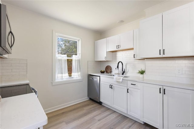 kitchen with appliances with stainless steel finishes, light hardwood / wood-style flooring, tasteful backsplash, white cabinets, and sink