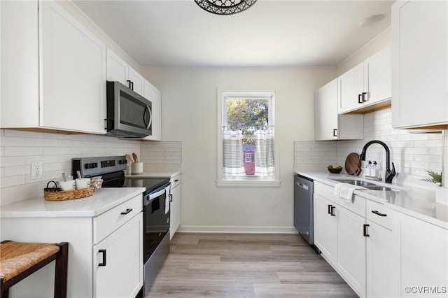 kitchen with sink, appliances with stainless steel finishes, white cabinetry, and light hardwood / wood-style flooring