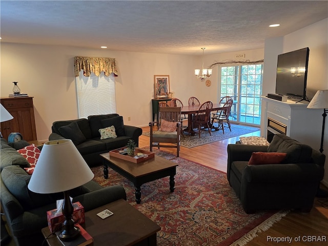 living room featuring a notable chandelier, a textured ceiling, hardwood / wood-style flooring, and a fireplace