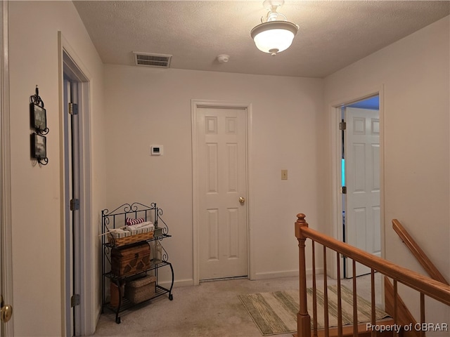 corridor with a textured ceiling and light colored carpet