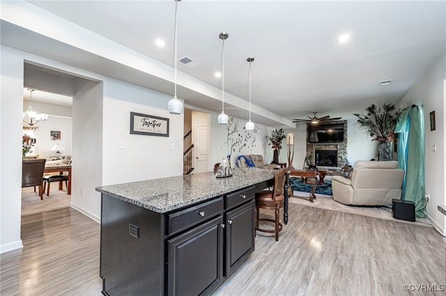 kitchen with a stone fireplace, hanging light fixtures, light stone countertops, a center island, and light wood-type flooring