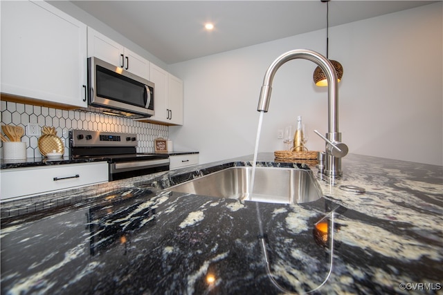 kitchen featuring dark stone counters, white cabinets, sink, decorative light fixtures, and stainless steel appliances