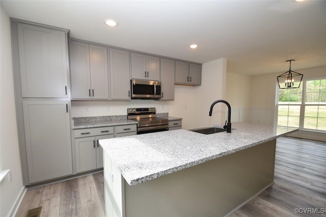 kitchen with light stone countertops, sink, light wood-type flooring, stainless steel appliances, and a kitchen island with sink