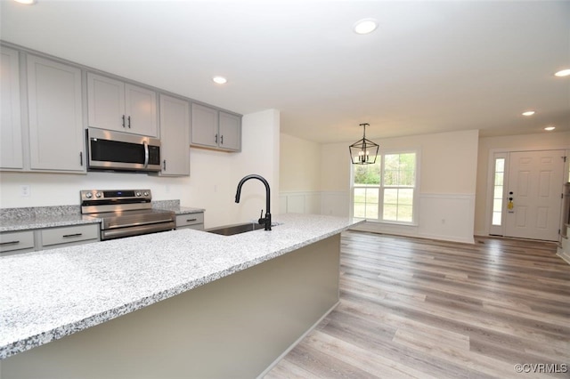 kitchen featuring a wainscoted wall, light wood finished floors, stainless steel appliances, gray cabinetry, and a sink