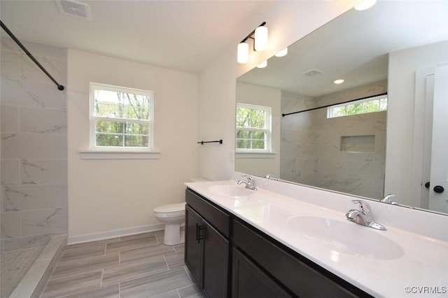 bathroom with a tile shower, toilet, vanity, and a wealth of natural light