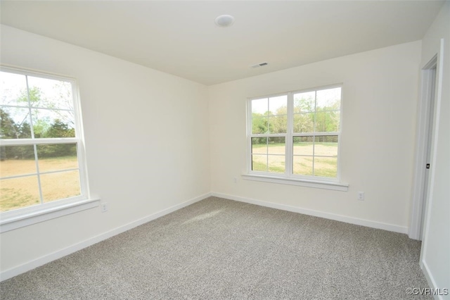 carpeted spare room with a wealth of natural light, visible vents, and baseboards