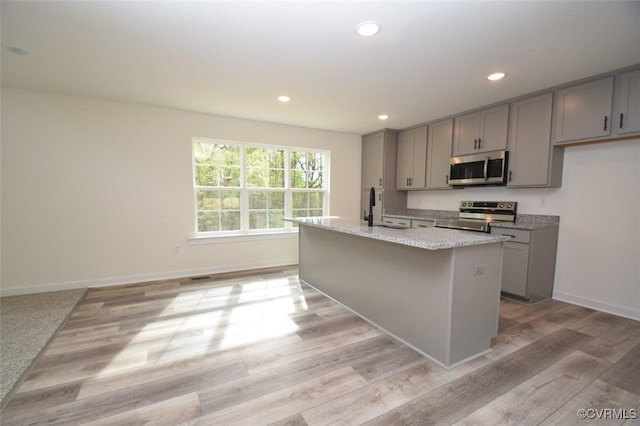 kitchen with gray cabinetry, stainless steel appliances, light hardwood / wood-style flooring, and an island with sink