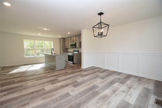 kitchen with a center island with sink, pendant lighting, gray cabinetry, light hardwood / wood-style floors, and stainless steel appliances