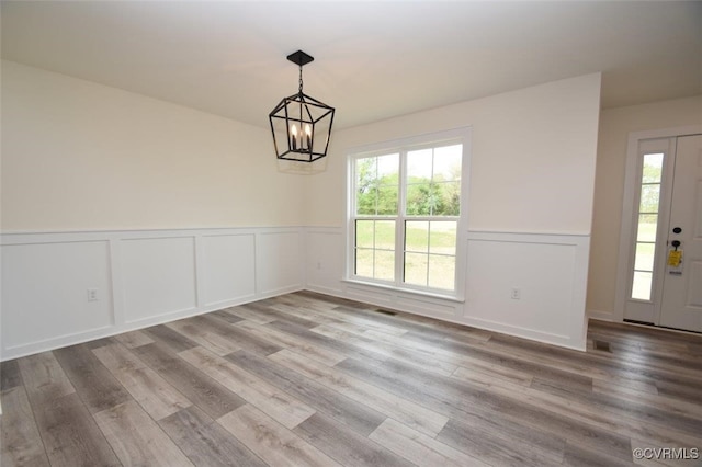 unfurnished dining area featuring wainscoting, visible vents, an inviting chandelier, and wood finished floors