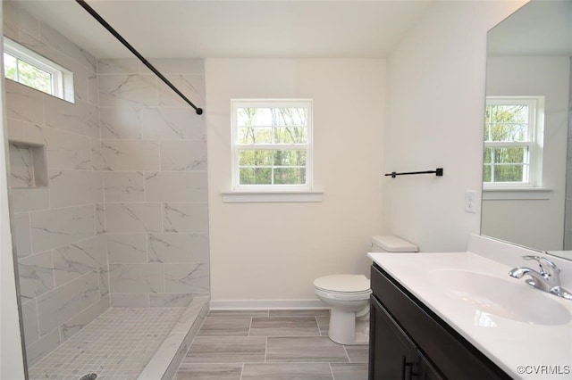 bathroom featuring toilet, baseboards, a tile shower, and vanity