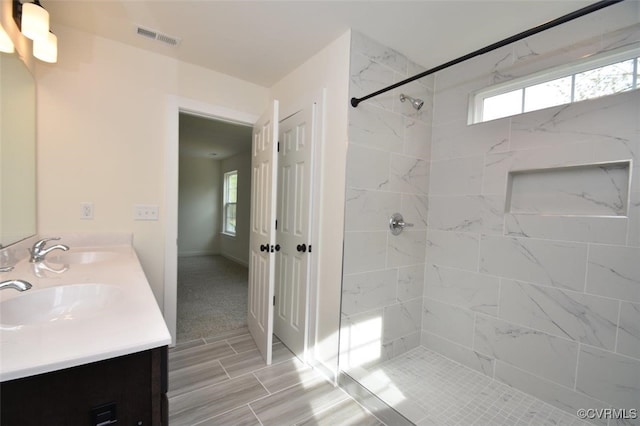 bathroom with visible vents, a sink, a tile shower, and double vanity