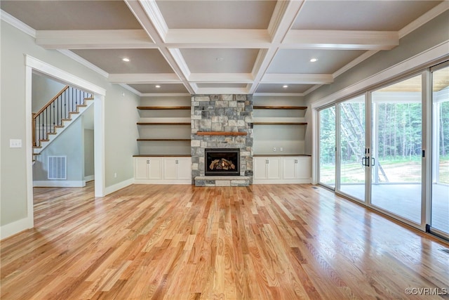 unfurnished living room featuring coffered ceiling, beam ceiling, a stone fireplace, and light hardwood / wood-style flooring