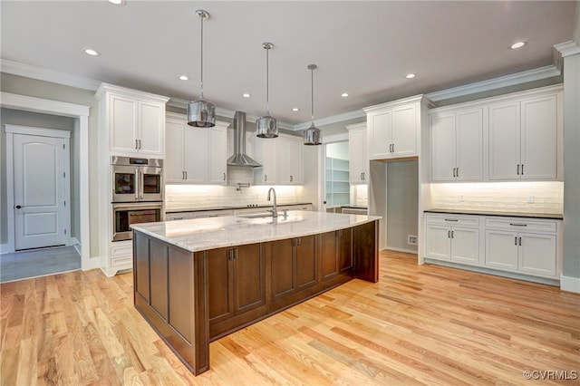 kitchen featuring white cabinets, double oven, and an island with sink