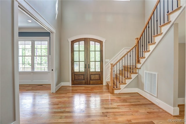 entryway with french doors, ornamental molding, a high ceiling, and light wood-type flooring