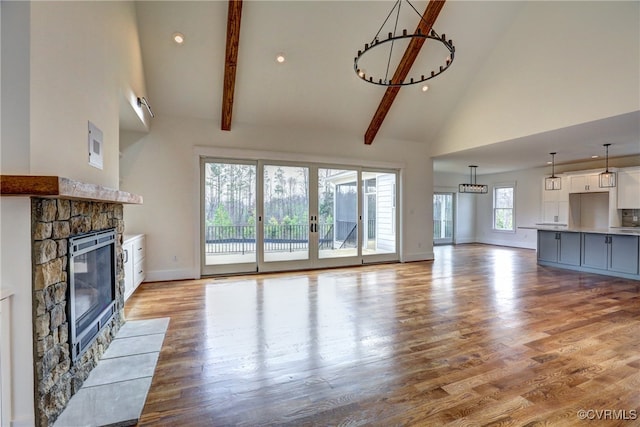 unfurnished living room featuring a stone fireplace, beamed ceiling, high vaulted ceiling, and light hardwood / wood-style floors