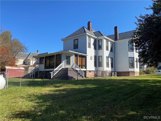 back of house featuring a chimney, fence, entry steps, a yard, and a sunroom