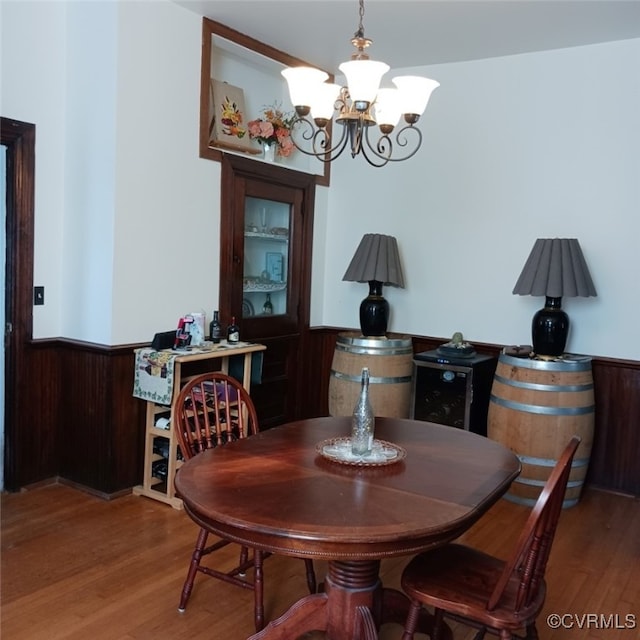 dining room featuring wooden walls, a notable chandelier, wainscoting, and wood finished floors