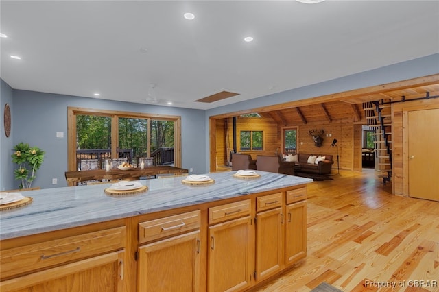 kitchen with light stone counters, vaulted ceiling with beams, wooden walls, and light wood-type flooring