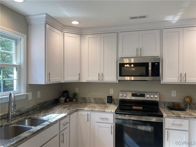 kitchen with appliances with stainless steel finishes, white cabinetry, sink, and light stone counters