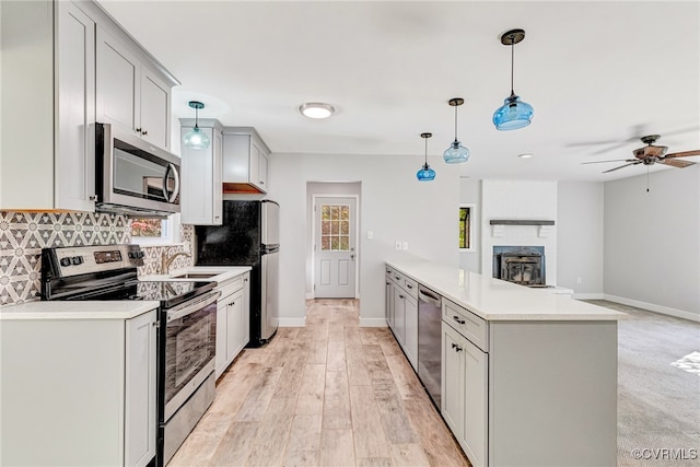 kitchen featuring sink, hanging light fixtures, light hardwood / wood-style floors, a fireplace, and appliances with stainless steel finishes