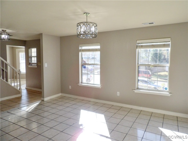 tiled spare room with a wealth of natural light and a chandelier