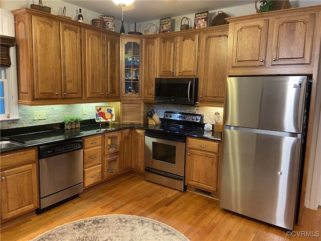 kitchen with dark stone countertops, light hardwood / wood-style floors, appliances with stainless steel finishes, and backsplash