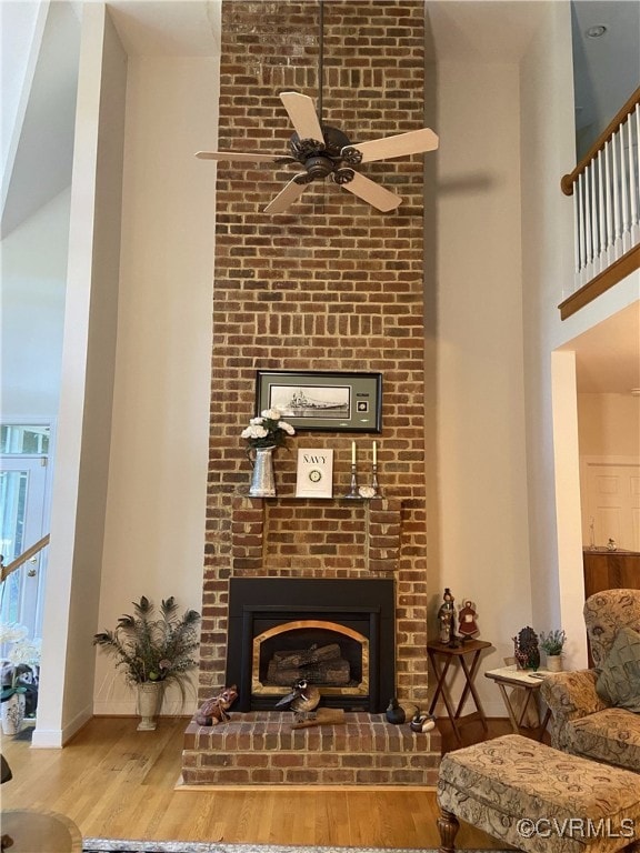 living room featuring a brick fireplace, wood-type flooring, and ceiling fan